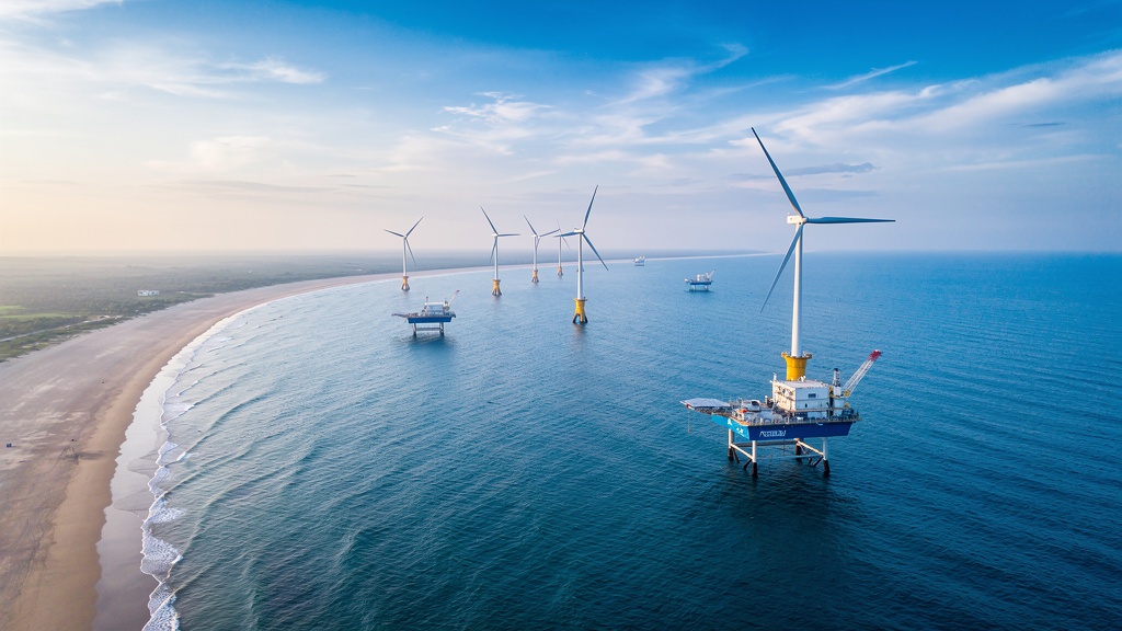 A pristine Indian coastline at low light, calm water lapping against pale sand, with no diesel plumes or visible pollution, evoking the clean-air dividend of marine renewables.