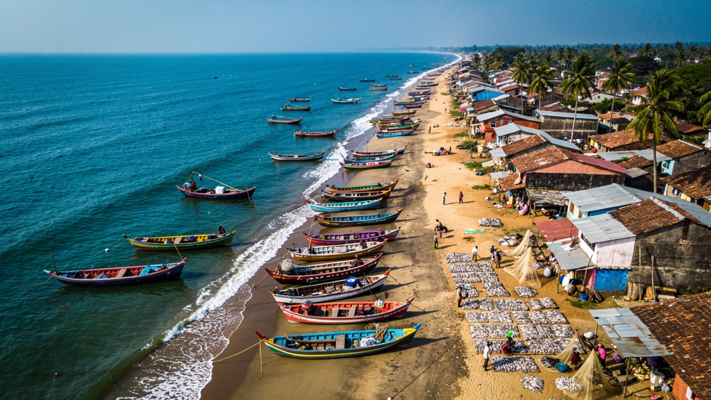 A row of traditional Indian fishing villages along a sandy coastline with catamarans pulled up on the beach at dawn.