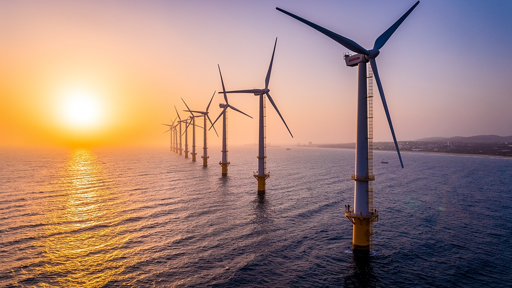 A row of offshore wind turbines standing in the Arabian Sea at sunset off India’s coast.