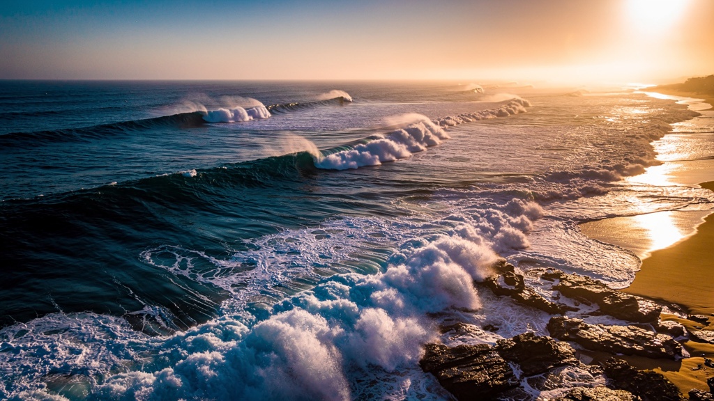 Aerial photograph of large rolling ocean waves breaking on the southern coast of India at golden hour.